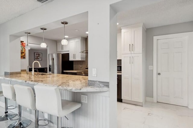 kitchen featuring pendant lighting, backsplash, kitchen peninsula, white cabinetry, and stainless steel fridge with ice dispenser