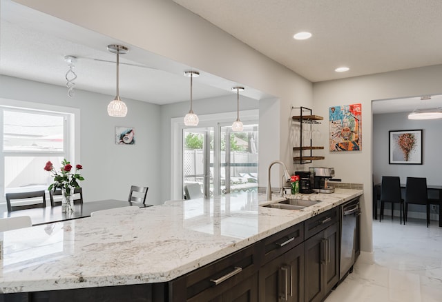 kitchen featuring hanging light fixtures, light stone countertops, sink, and a kitchen island with sink