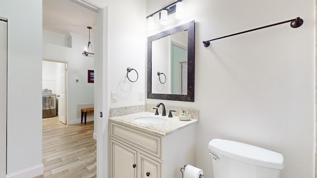 bathroom featuring vanity, crown molding, hardwood / wood-style flooring, washer / dryer, and toilet