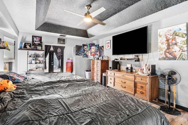 bedroom with a raised ceiling, ceiling fan, a textured ceiling, and hardwood / wood-style flooring