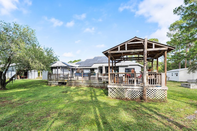 back of property featuring solar panels, a yard, a deck, and a storage shed