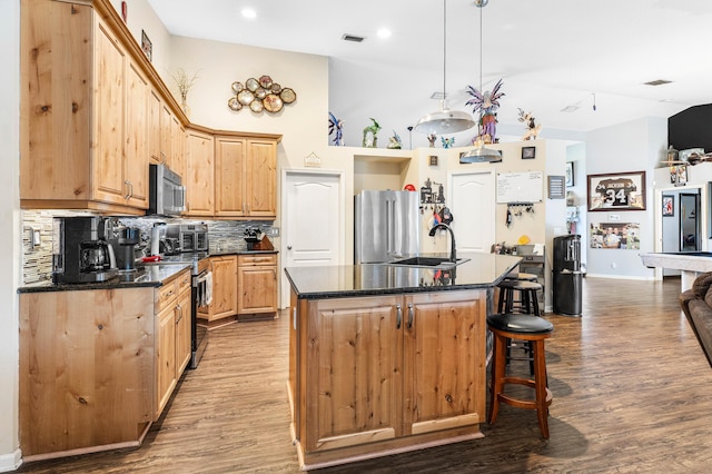 kitchen with light wood-type flooring, appliances with stainless steel finishes, backsplash, and a kitchen island with sink