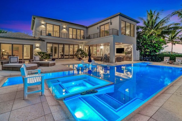 pool at dusk featuring an in ground hot tub, an outdoor living space, and a patio