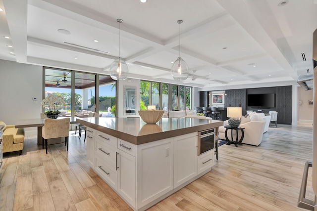 kitchen featuring coffered ceiling, white cabinetry, hanging light fixtures, and light hardwood / wood-style flooring