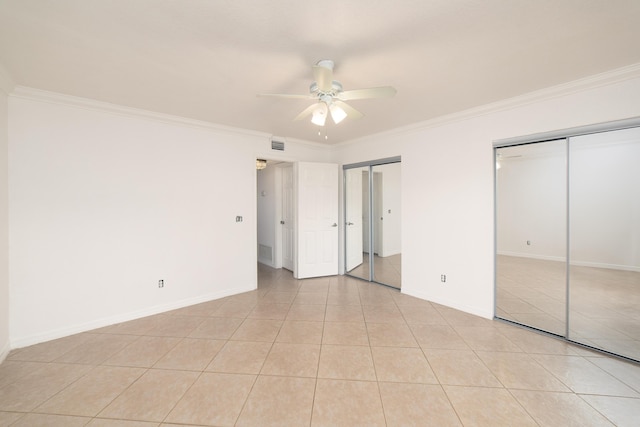 unfurnished bedroom featuring two closets, ceiling fan, crown molding, and light tile patterned flooring