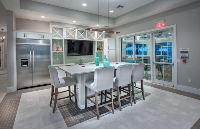 kitchen featuring decorative light fixtures, a kitchen island, built in fridge, a breakfast bar area, and white cabinetry