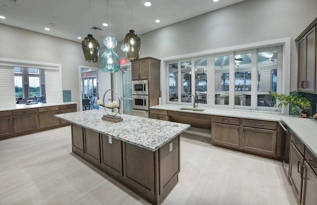 kitchen featuring a kitchen island, stainless steel microwave, light stone countertops, and sink