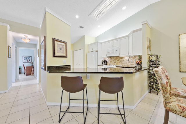 kitchen featuring white appliances, white cabinets, vaulted ceiling, light tile patterned floors, and kitchen peninsula