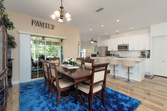 dining space with light wood-type flooring, ceiling fan with notable chandelier, a wealth of natural light, and sink