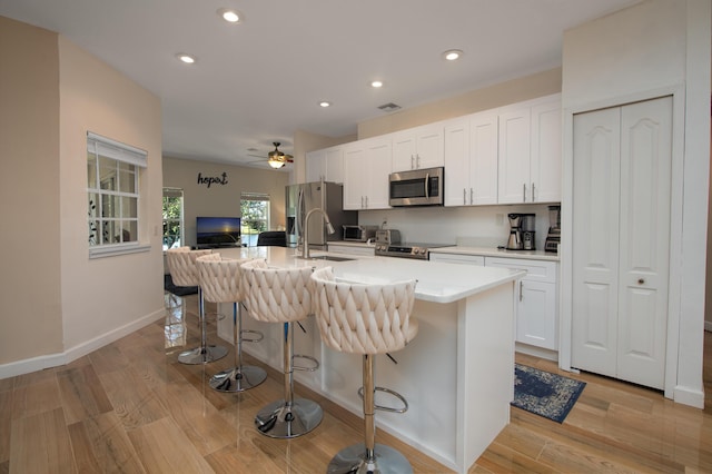 kitchen with a breakfast bar, sink, an island with sink, appliances with stainless steel finishes, and white cabinetry