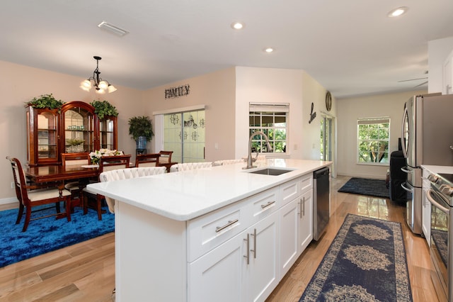 kitchen with light wood-type flooring, sink, a center island with sink, white cabinetry, and hanging light fixtures