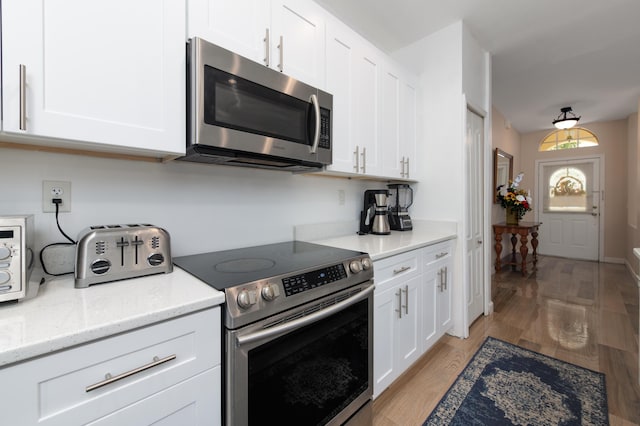 kitchen featuring appliances with stainless steel finishes, light hardwood / wood-style flooring, white cabinetry, and light stone counters