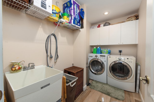 laundry room with washing machine and dryer, cabinets, sink, and light hardwood / wood-style floors