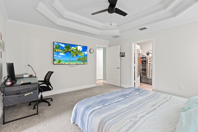 carpeted bedroom featuring a tray ceiling, a spacious closet, ceiling fan, and crown molding