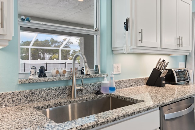 kitchen with stainless steel dishwasher, plenty of natural light, white cabinetry, and sink