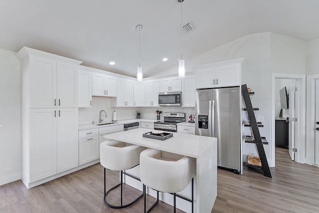 kitchen featuring lofted ceiling, sink, appliances with stainless steel finishes, decorative light fixtures, and white cabinetry