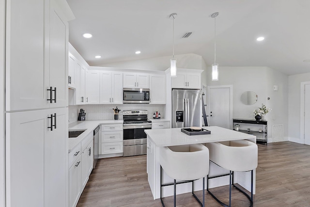 kitchen featuring stainless steel appliances, pendant lighting, lofted ceiling, decorative backsplash, and white cabinets