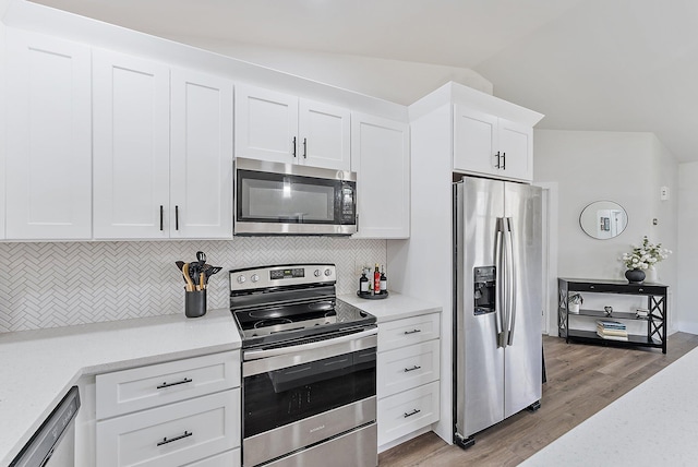 kitchen featuring dark wood-type flooring, vaulted ceiling, decorative backsplash, appliances with stainless steel finishes, and white cabinetry