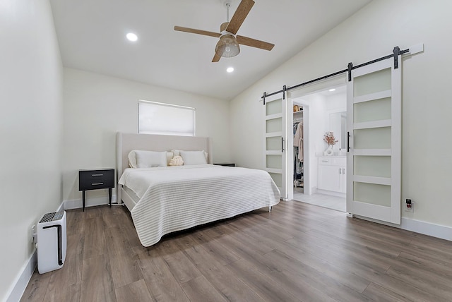 bedroom featuring ceiling fan, a barn door, vaulted ceiling, a walk in closet, and a closet