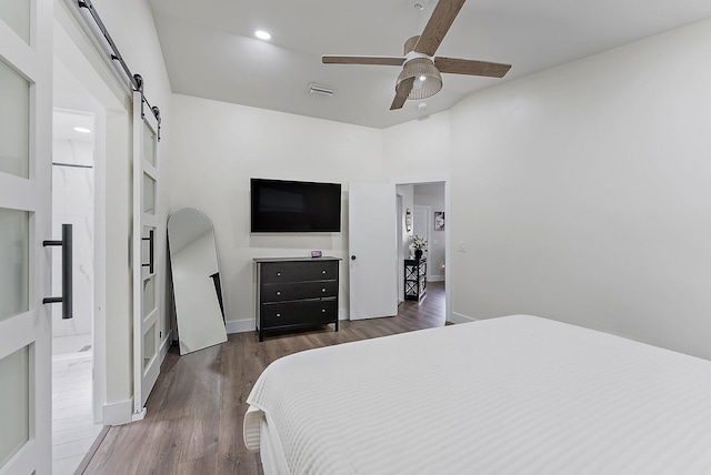 bedroom with ceiling fan, a barn door, and dark hardwood / wood-style floors