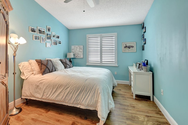 bedroom with vaulted ceiling, ceiling fan, a textured ceiling, and light wood-type flooring