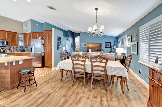 dining area with light wood-type flooring, lofted ceiling, and a notable chandelier