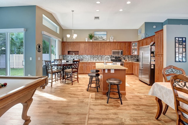 kitchen with appliances with stainless steel finishes, tasteful backsplash, pendant lighting, a notable chandelier, and an island with sink