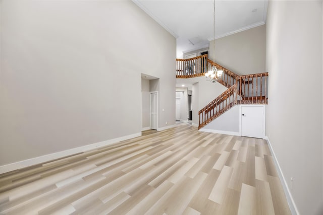 unfurnished living room with a chandelier, a towering ceiling, light hardwood / wood-style floors, and crown molding