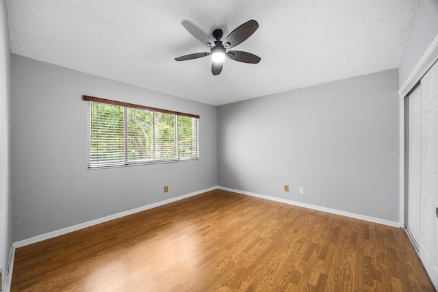 unfurnished bedroom featuring ceiling fan, a closet, wood-type flooring, and a textured ceiling