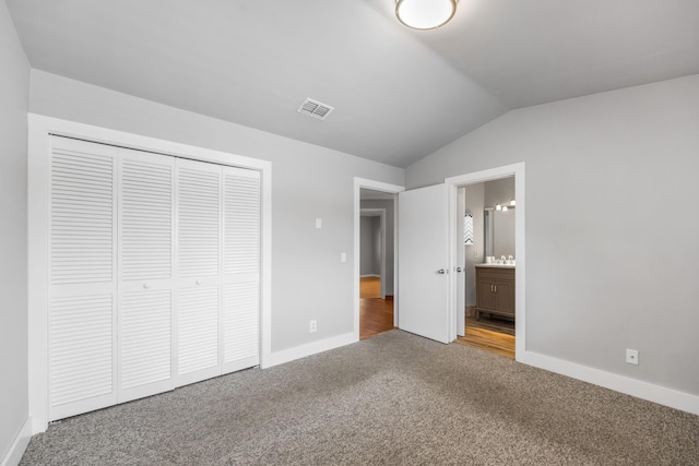 unfurnished bedroom featuring carpet floors, a closet, lofted ceiling, and connected bathroom