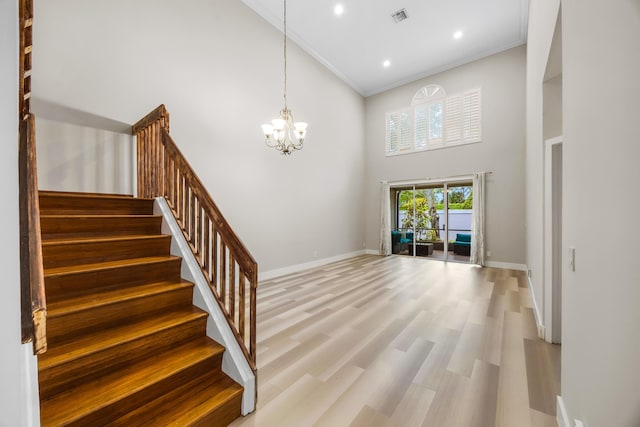 foyer with hardwood / wood-style floors, a towering ceiling, crown molding, and an inviting chandelier