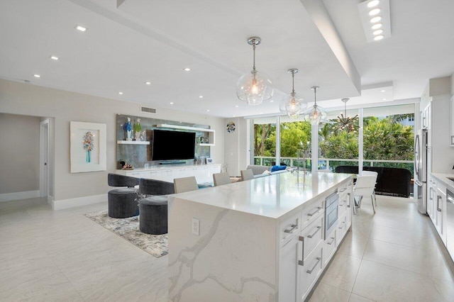 kitchen featuring hanging light fixtures, a large island, light stone counters, white cabinetry, and stainless steel appliances