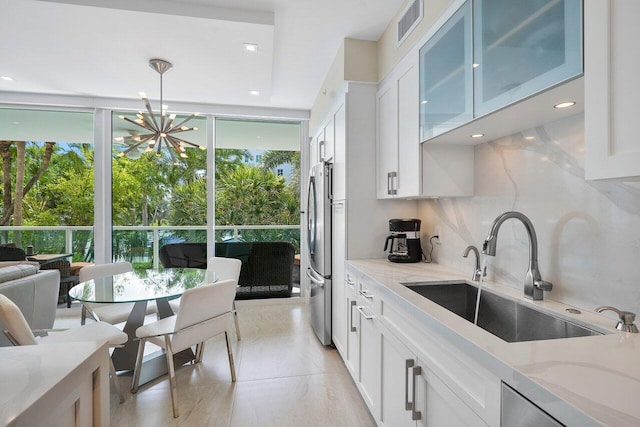 kitchen featuring white cabinets, sink, tasteful backsplash, decorative light fixtures, and stainless steel refrigerator