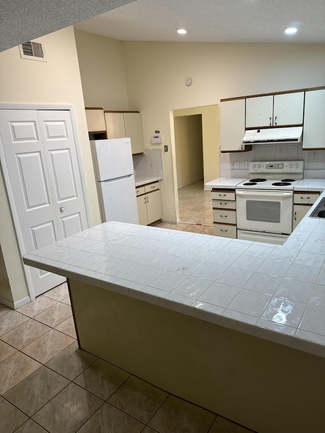 kitchen featuring tile counters, vaulted ceiling, white appliances, decorative backsplash, and light tile patterned floors