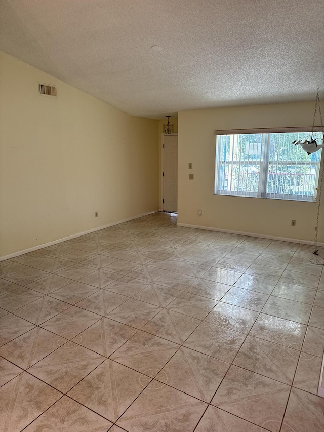 tiled empty room with a chandelier and a textured ceiling