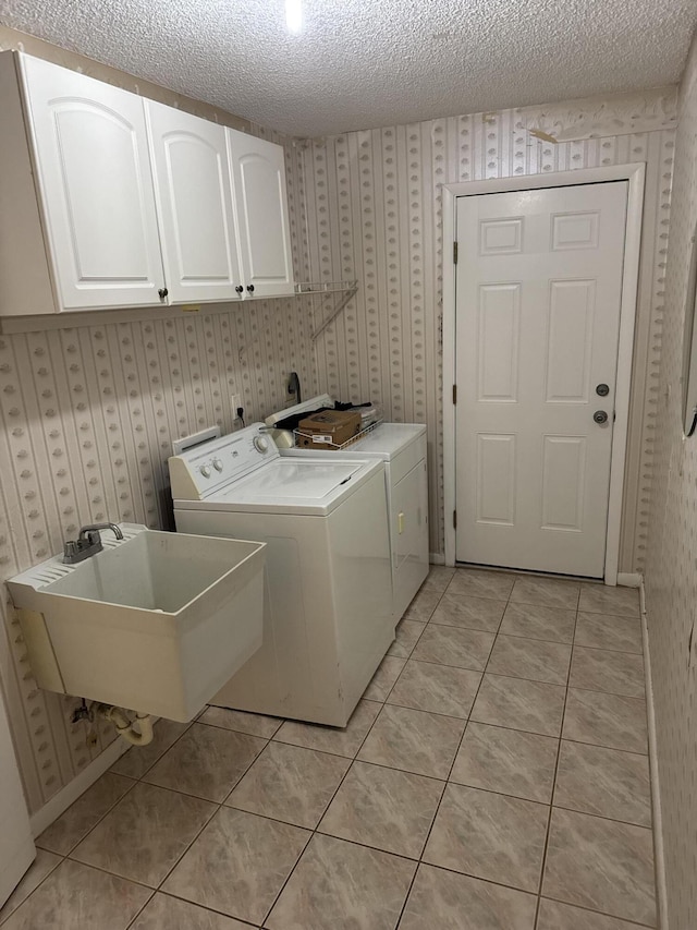 clothes washing area featuring cabinets, sink, washing machine and dryer, a textured ceiling, and light tile patterned flooring