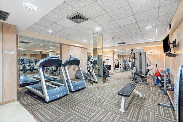 workout area with wooden walls and a drop ceiling