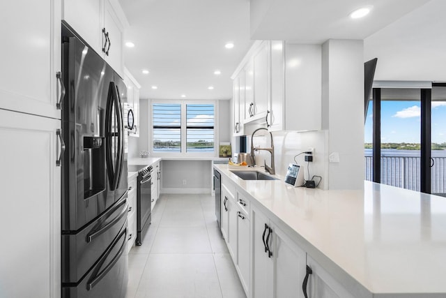 kitchen with a water view, stainless steel appliances, white cabinetry, light tile patterned flooring, and sink