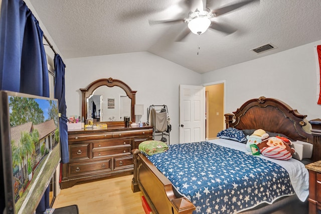 bedroom featuring a textured ceiling, light wood-type flooring, vaulted ceiling, and ceiling fan