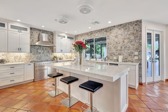 kitchen with appliances with stainless steel finishes, a breakfast bar, tasteful backsplash, a center island, and wall chimney range hood