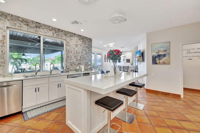 kitchen featuring a kitchen island, white cabinetry, a breakfast bar area, stainless steel dishwasher, and light tile patterned floors