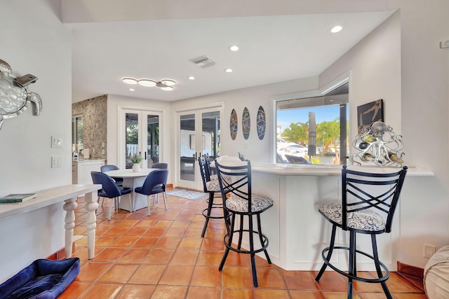 kitchen with plenty of natural light, light tile patterned flooring, a breakfast bar, and french doors