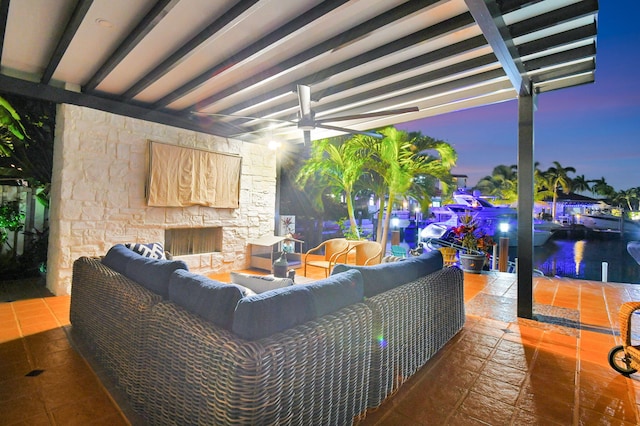 patio terrace at dusk featuring a water view, ceiling fan, and an outdoor living space with a fireplace