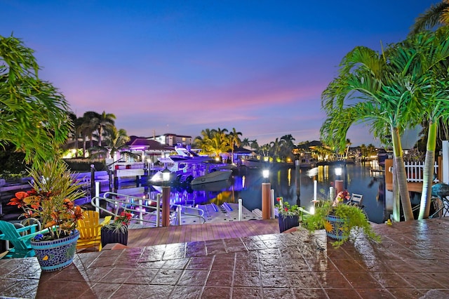 patio terrace at dusk featuring a water view and a dock