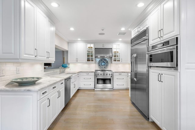 kitchen featuring decorative backsplash, light stone counters, light hardwood / wood-style flooring, high quality appliances, and white cabinetry