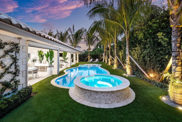 pool at dusk with a lawn, a patio area, and an in ground hot tub