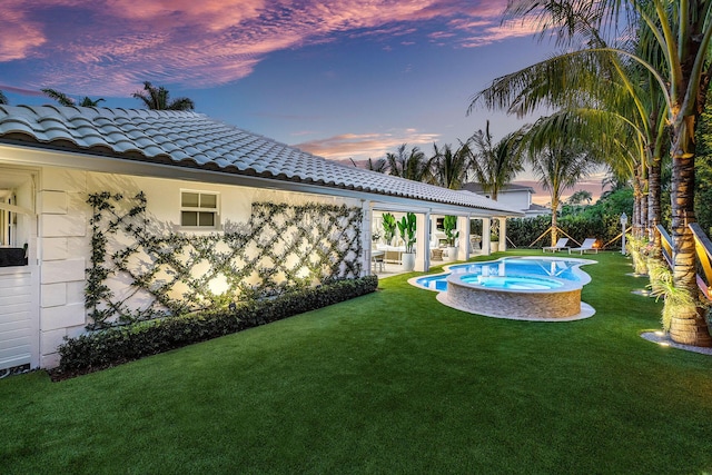 pool at dusk with an in ground hot tub, a yard, and a patio