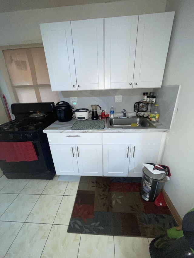 kitchen featuring white cabinets, black gas stove, light tile patterned flooring, and sink