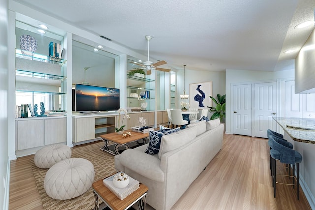 living room with light wood-type flooring, built in shelves, a textured ceiling, ceiling fan, and lofted ceiling