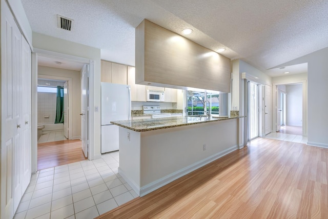 kitchen with kitchen peninsula, dark stone counters, white appliances, a textured ceiling, and light tile patterned floors